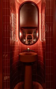 Bathroom with red walls, a metal sink, and two mirrors, creating a warm and inviting atmosphere