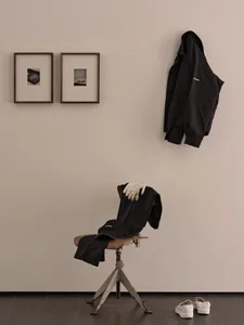 A home office with a white wall featuring two framed pictures and a chair with two black jackets and a handbag