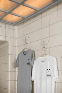 A bathroom with two hanging t-shirts, one with a tennis racket design and one plain white, against a tile wall