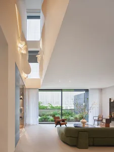 Open living area with two couches, a chair, and a potted plant, surrounded by white walls and floors, with natural light from a large window