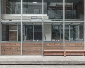 A modern building with a large glass wall and two benches inside, surrounded by natural light