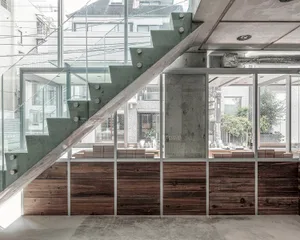 A modern building with a wooden staircase, large windows, potted plants, and decorative vases, set against a bright and airy background