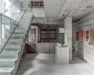 Open living area with concrete walls, a variety of furniture, and decorative bottles, set against a modern and industrial backdrop