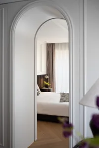 Cozy bedroom with a white bed, black pillows, and ample lighting from two lamps and large windows