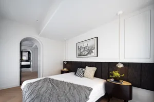 Cozy bedroom with a large bed, black headboard, and nightstands, featuring a potted plant and a white wall