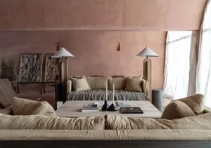 A modern living area with a pinkish hue, featuring a couch, table, chairs, and wooden furniture, lit by two lamps and providing a comfortable environment for relaxation and socializing