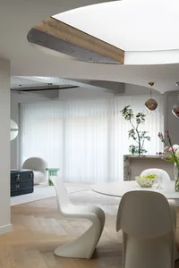 Cozy open concept living space with a dining table, two white chairs, a bowl, and potted plants