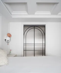 A calm and inviting bedroom with a white bed, metal-framed window, and white plaster walls