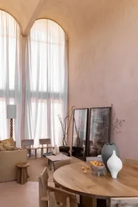 A modern living room with a couch, chairs, tables, vases, and potted plants, featuring neutral tones and minimalistic decorations