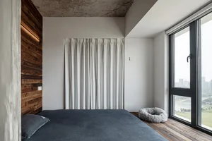Cozy bedroom with a gray blanket-covered bed near a window, two pillows, and natural light