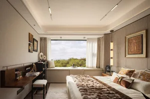 Cozy bedroom with a white fur throw, large window, two chairs, and a dining table, offering a luxurious and comfortable living environment