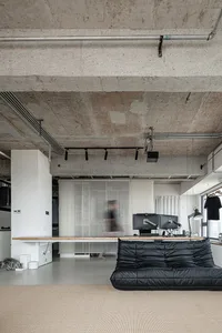 現代客廳區，靠近窗邊的黑色沙發、兩把椅子、電視與餐桌，空間內有一人站立