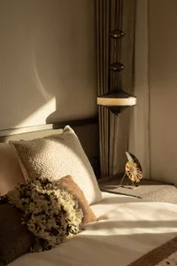 A cozy bedroom with a large bed, pillows, and a lamp on a nightstand, surrounded by soft lighting and comfortable furnishings