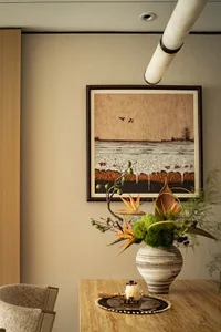 A still life scene featuring a vase with flowers on a table in front of a picture frame with a coastal painting