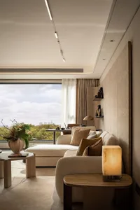 A city-view living room with two couches, a chair, a dining table, potted plants, and a vase, set against a backdrop of a large window and a cityscape outside