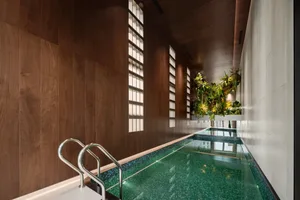 A swimming pool area with a green tiled bottom, wood paneling on the walls, and natural light from a large window