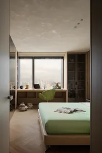 Cozy modern bedroom with a green bed near a large window offering a city view, surrounded by books and a chair