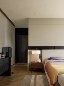 A modern bedroom with a large bed, two nightstands, and a clock, set against a white-painted wall in a clean and minimalist space