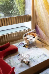 A woman plays the piano in a cozy living area with a grand piano, couches, and chairs, creating a warm and inviting atmosphere