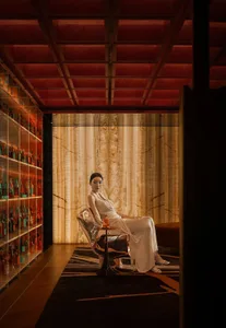 A woman sits in a chair in a well-decorated living area with bottles and wine glasses, conveying a sense of comfort and refinement