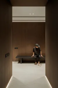 A man sits on a bench in a dark room with wooden walls and flooring, giving it an old and rustic feel
