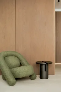 A modern interior design featuring a green chair in front of a wooden wall, with two tables and a minimalist atmosphere