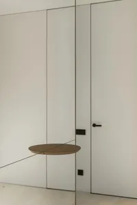 A white room with a brown door, a mirror, and a decorative piece above the door, creating a clean and minimalistic atmosphere
