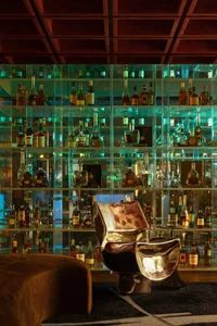 A cozy bar area with glass shelves displaying a collection of liquor bottles and a chair for seating, set in a relaxed environment