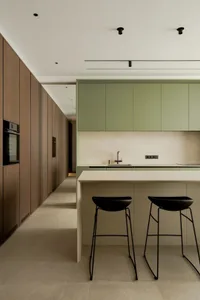 Modern kitchen with white countertops, green cabinets, and black stools, featuring clean lines and minimalistic design