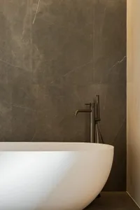 A modern bathroom with a large white bathtub in front of a gray wall, featuring two faucets and an elegant design
