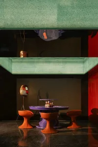 A purple circular dining table surrounded by orange chairs in a room with a green wall, creating a vibrant and unique atmosphere