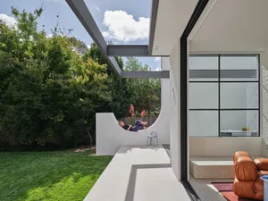 A man relaxes on a chair outside a house with a glass door, surrounded by a patio and a bench in a calm and serene atmosphere