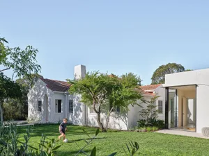A white house with a green lawn and a patio with a dining table and chairs, surrounded by a relaxed family-oriented atmosphere