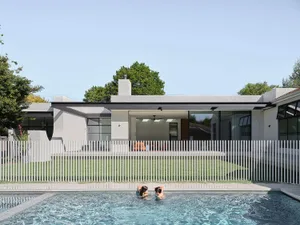 a modern house with a gray exterior and a well-maintained pool area with a fence and two people swimming