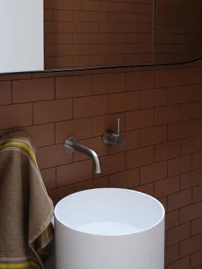 Bathroom with a white porcelain sink mounted on a brown brick wall with a tiled design and two faucets, accompanied by a towel