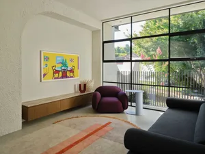 Bright and inviting living area with wooden furniture, white walls, and a large window allowing natural light to enter