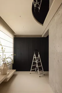 A clean and organized living area with a white wall, a black doorway, and a vase near the bottom left corner, featuring two ladders and a sense of minimalism