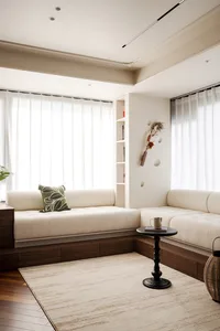 Cozy living room with a couch against a white wall, natural light from two windows, and wooden floors, with a potted plant adding a touch of greenery