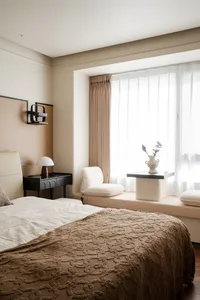 Bright and inviting bedroom with two beds, a chair, dresser, and vase, lit by natural light from a large window