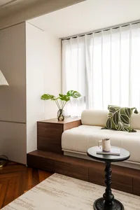 Cozy living room with a couch in front of a window, surrounded by potted plants, a vase, and a cup, with natural light and inviting atmosphere