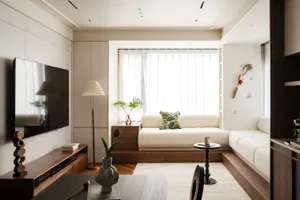 A modern living area with a white couch, wooden furniture, and a dining table near a window, filled with natural light