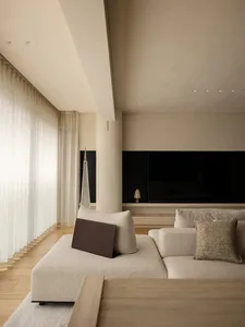 A well-lit modern living area with a large couch, two chairs, and pillows, surrounded by natural light from windows