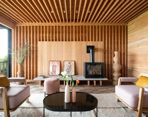 Cozy living space with a fireplace, couch, chairs, and dining table, lit by natural sunlight through windows