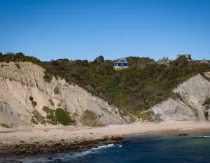 A serene beach house with a wooden exterior, blue roof, and stunning ocean views from a cliffside location