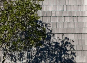 A serene house with a gray roof and a tree in front, casting a shadow on the wall, surrounded by sunlight
