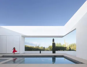 A modern indoor pool area with a large pool surrounded by white walls and potted plants, creating a serene ambiance