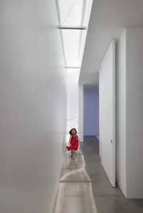 A young girl in a red dress walks down a white hallway with no other objects or people present