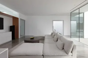 Empty living room with a large couch and two chairs, well-lit with natural sunlight through windows