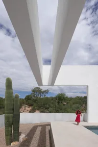 Modern desert building with a bridge-like structure, surrounded by cacti and a person in the foreground