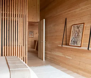 Warm and inviting bedroom with wooden walls and floors, featuring two beds and a doorway leading to other parts of the house